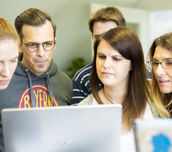 ABM. Mehrere Personen stehen zusammen und schauen auf einen Laptop.