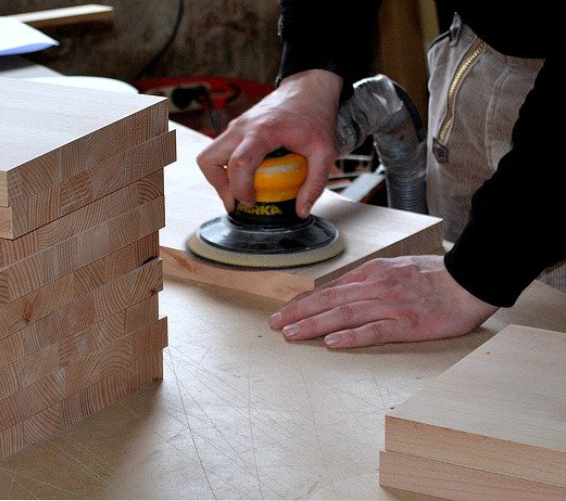 Holz. Technikraum. Werkbar. Person in einer Werkstatt streicht Holzlatten mit einem Pinsel.