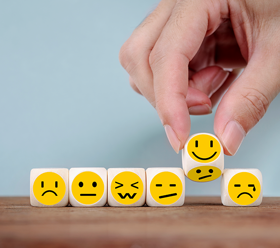 Psychische Belastung. Person reiht Würfel aneinander. Auf den Würfeln sind Emojis mit verschiedenen Emotionen zu sehen.