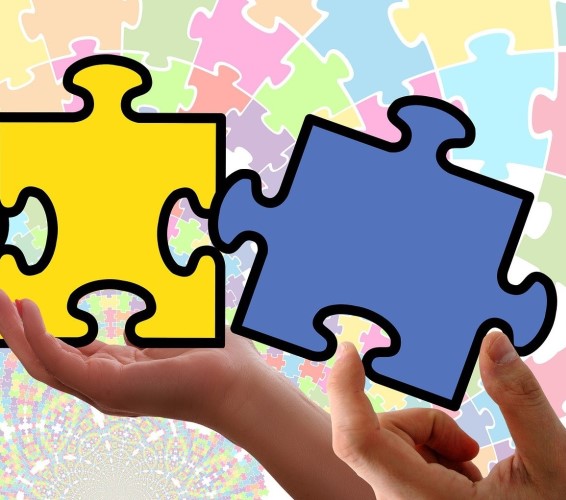 Integration. Zwei Hände setzen zwei große Puzzleteile zusammen.