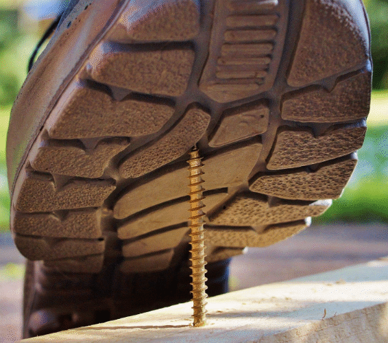 Arbeitssicherheit. Person tritt mit einem Schuh, auf eine Schraube.