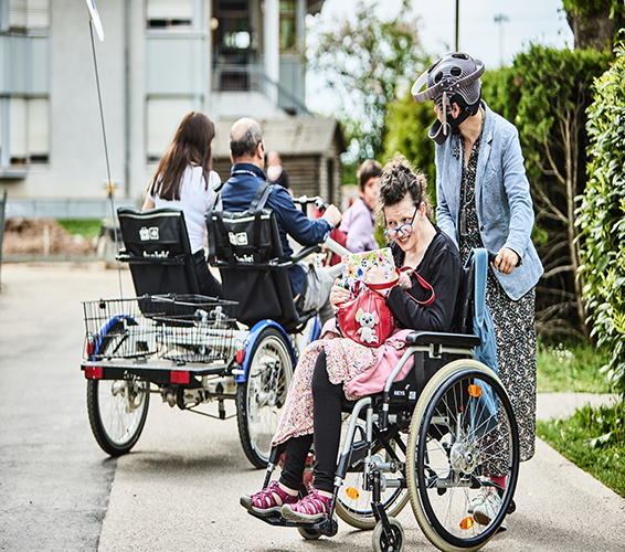 HPF. Mehrere Personen mit Rollstuhl, Fahrrad und zu Fuß.